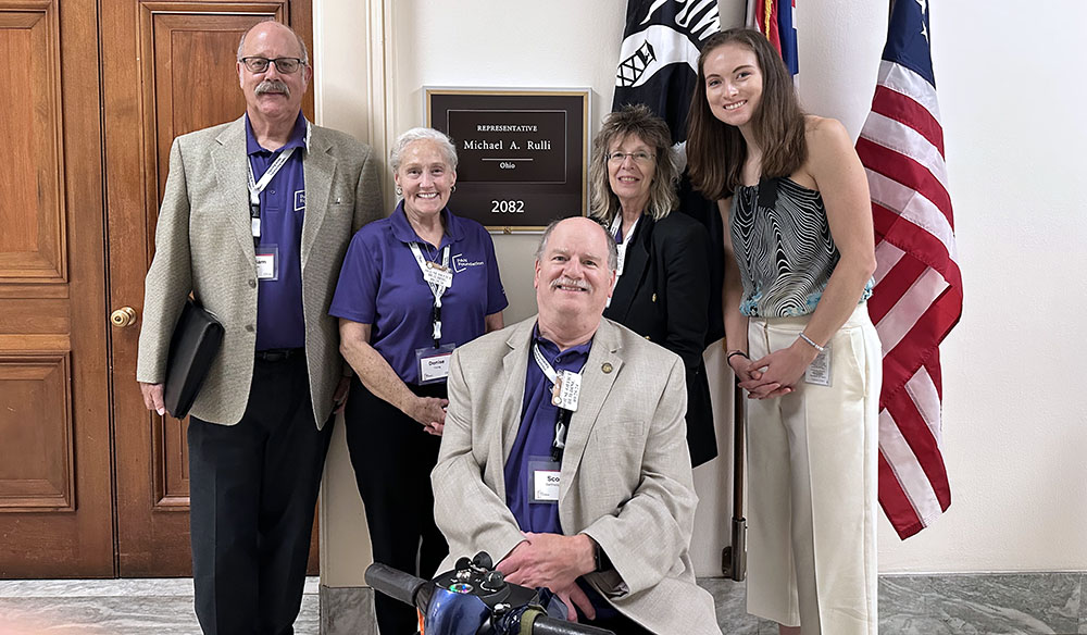 Scott poses with his wife, PAN advocates, and representatives in front of a Congressional office and flags at the PAN advocacy action summit